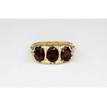 A 9ct yellow gold ring set with three oval cut garnets, (Q).