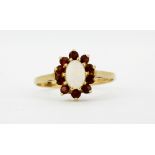 A hallmarked 9ct gold ring set with an oval cut opal surrounded by garnets, (M.5).