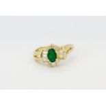 A 14ct yellow gold (stamped 14k) ring set with an oval cut emerald surrounded by round and