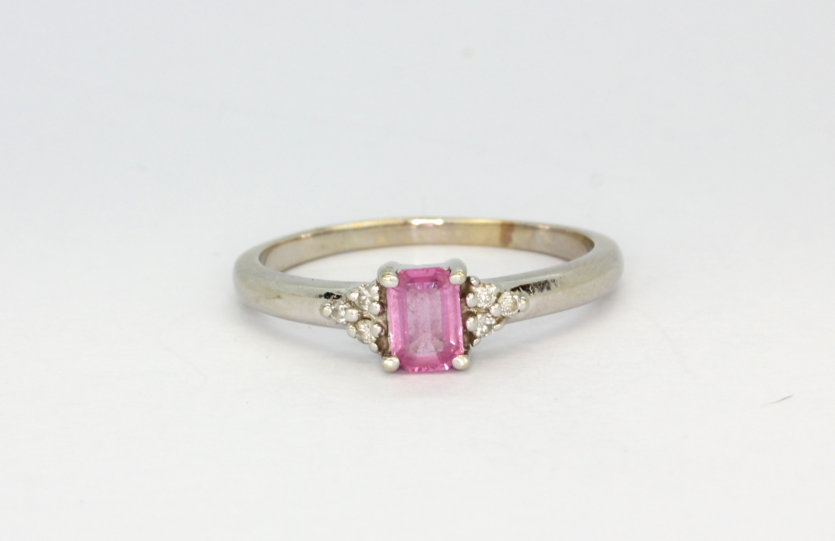 A 14ct white gold (stamped 14k) solitaire ring set with an emerald cut pink sapphire and diamond set