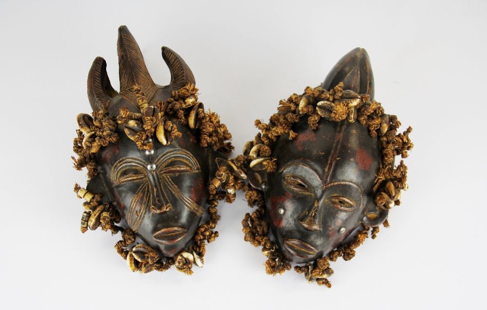 A pair of African clay and cowrie shell masks, H. 22cm.