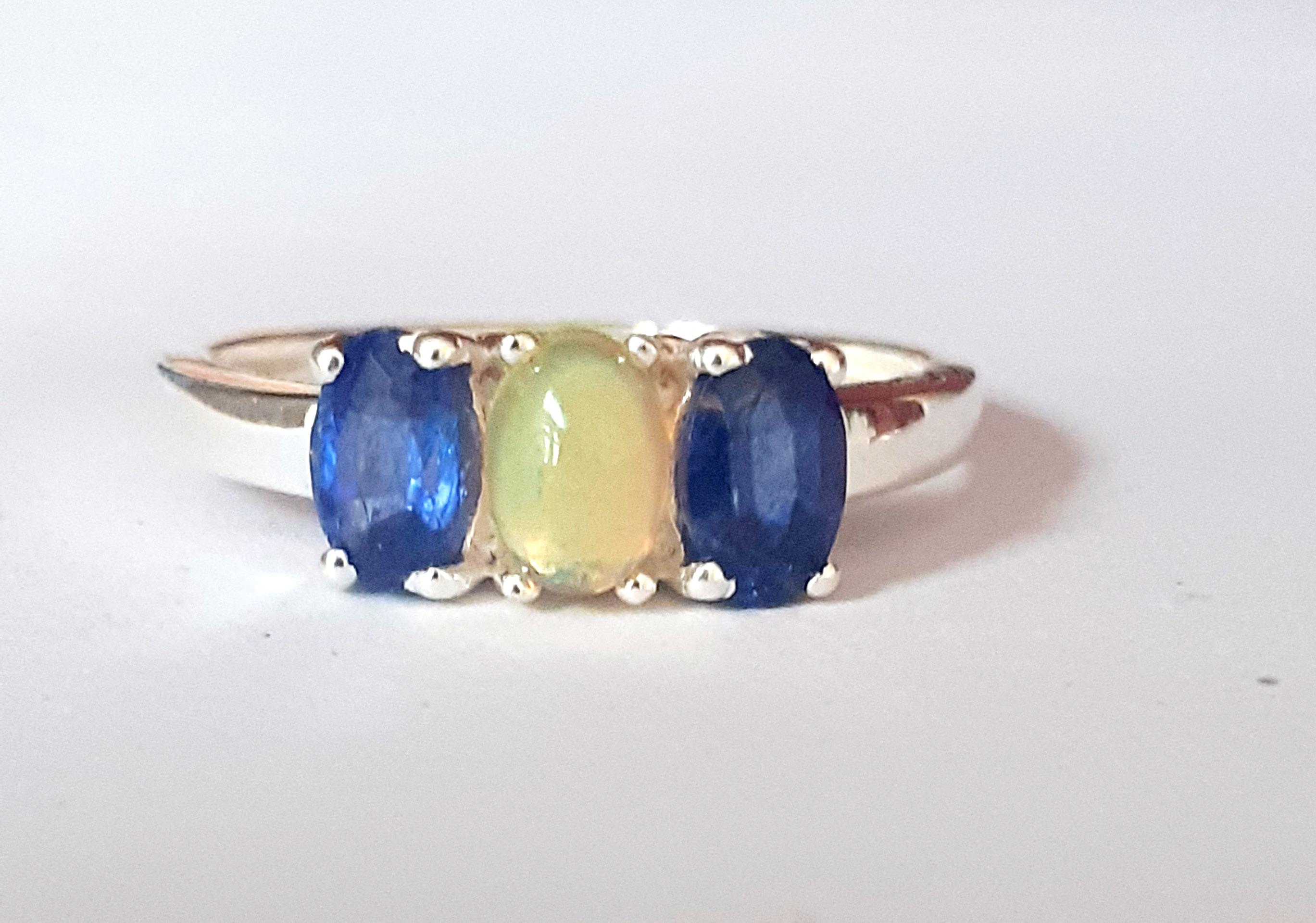 A 925 silver ring set with a cabochon cut opal flanked by oval cut sapphires, (P.5).