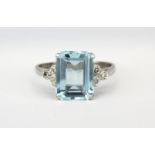 An 18ct white gold ring set with an emerald cut aquamarine and diamond set shoulders, (M.5).