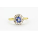 An 18ct yellow and white gold cluster ring set with an oval cut cornflower sapphire surrounded by