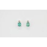 A pair of 9ct white gold stud earrings set with an oval cut emerald and a brilliant cut diamonds,