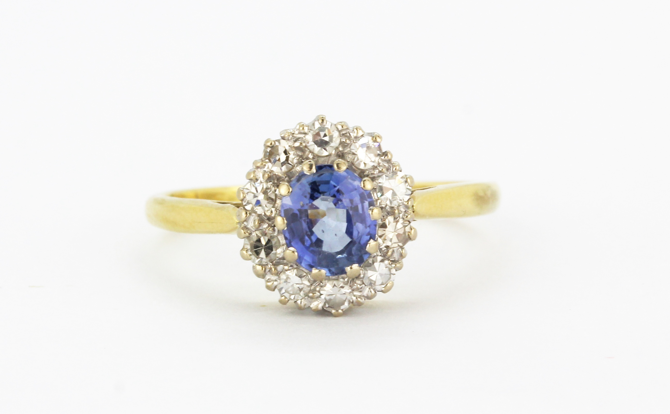 An 18ct yellow and white gold cluster ring set with an oval cut cornflower sapphire surrounded by