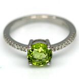 A 925 silver ring set with a round cut peridot and white stone set shoulders, (N.5).
