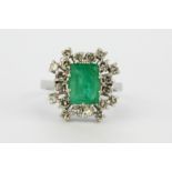 A white metal (tested 18ct gold) ring set with an emerald cut emerald surrounded by diamonds, (P).
