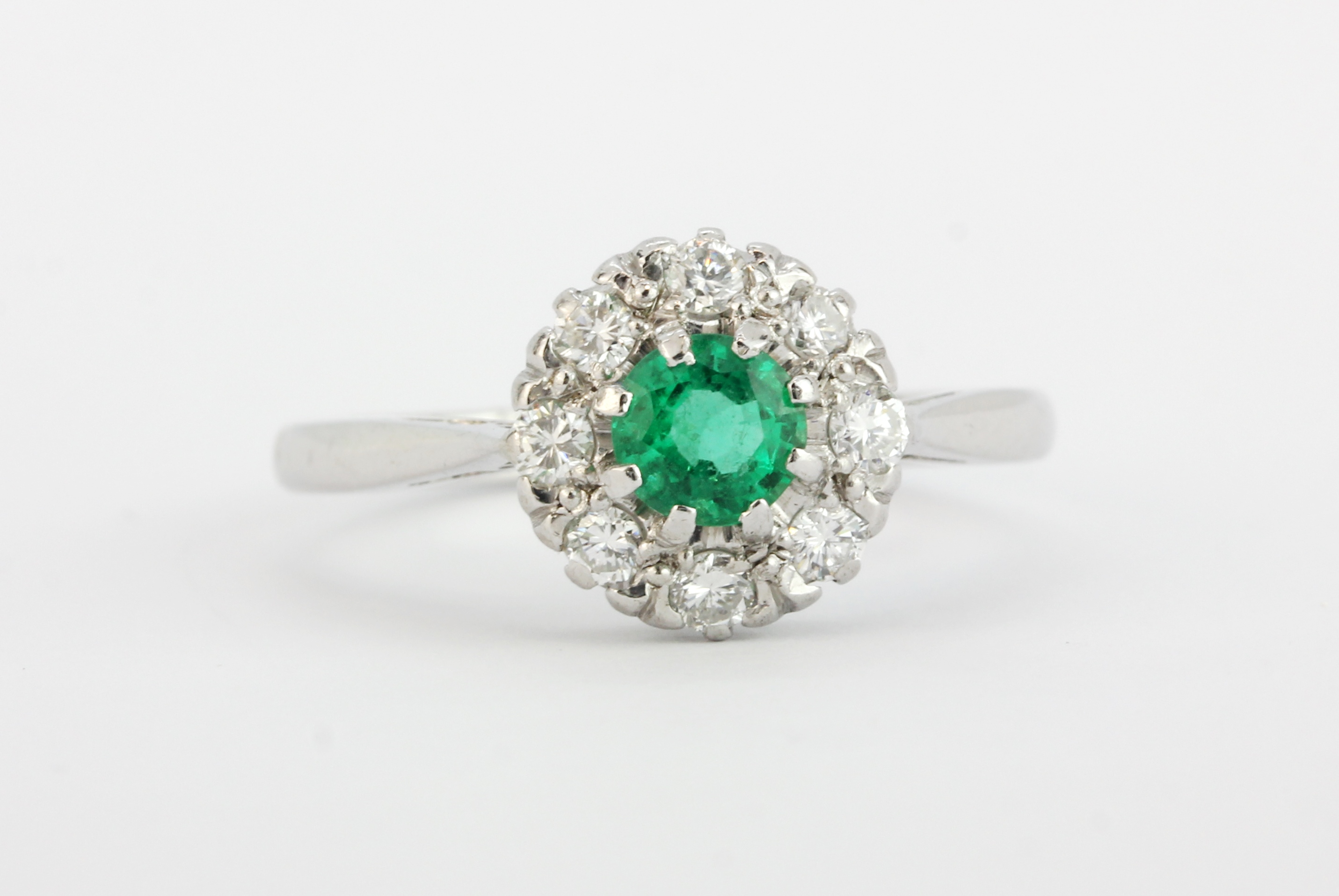 An 18ct white gold and platinum cluster ring set with a round cut emerald surrounded by brilliant