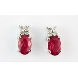 A pair of 9ct white gold (stamped 9k) stud earrings each set with an oval cut ruby and diamonds,