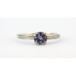 A hallmarked 9ct white gold ring set with a round cut tanzanite and diamond set shoulders, (U).