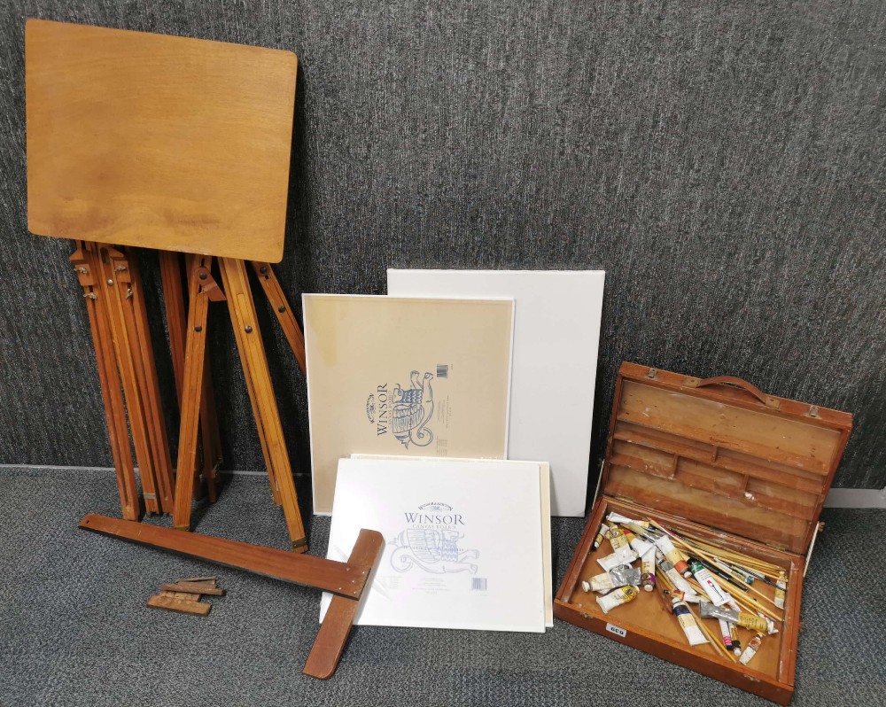 An artist easel, table, paint box and canvases.