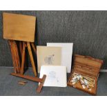 An artist easel, table, paint box and canvases.