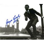 James Bond George Lazenby signed 10 x 8 inch b/w photo gum in hand with Houses of Parliament in