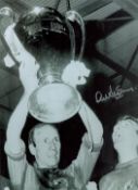 Football. Alex Stepney Hand signed 16x12 black and white photo. Photo shows Stepney holding aloft