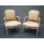 A pair of French painted frame fauteuils, floral cresting, scroll end arms, faded upholstery to