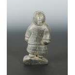 An Inuit carved greenstone figure of a hunter, circa 1960-70, standing in skins, on an angled