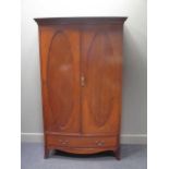 An Edwardian cross banded mahogany bow front two door wardrobe over a base drawer on outswept