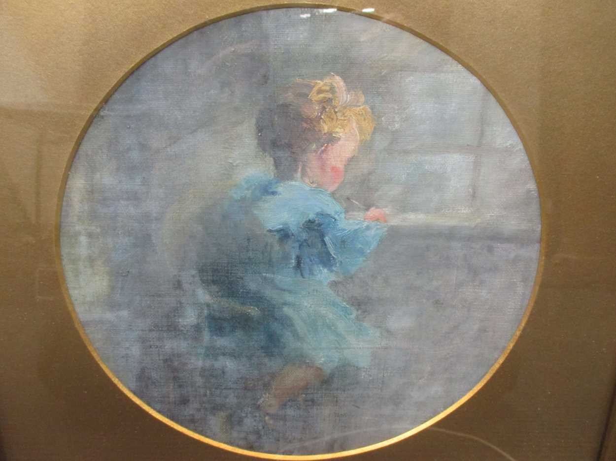 An early 20th century oil study of a young child writing, circular, probably on canvas board, 22cm