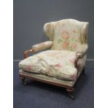 A 20th century walnut low armchair, with floral upholstery, shepherds crook arms and brass castors