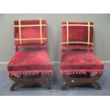 A near pair of low easy chairs upholstered in red velvet with tasselled fringe on x pattern support