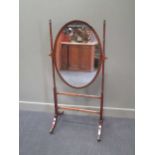 A Regency ring turned mahogany frame oval cheval mirror, circa 1820, on brass leaf capped sabre