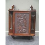 An Arts and Crafts oak and walnut hanging single door cupboard with birds and foliate decoration