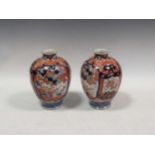 A pair of early 20th Century Japanese Imari vases painted with garden reserves alternating with