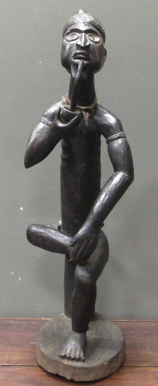 A 20th century African carved figure of seated male smoking a pipe, mirror insert to the side of the