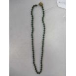 A necklace of nephrite jade beads with a yellow metal push-in clasp, unhallmarked, stamped '585