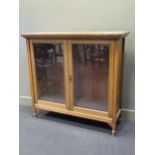 An Edwardian blonde oak bookcase with a carved dental cornice above two glazed doors on turned