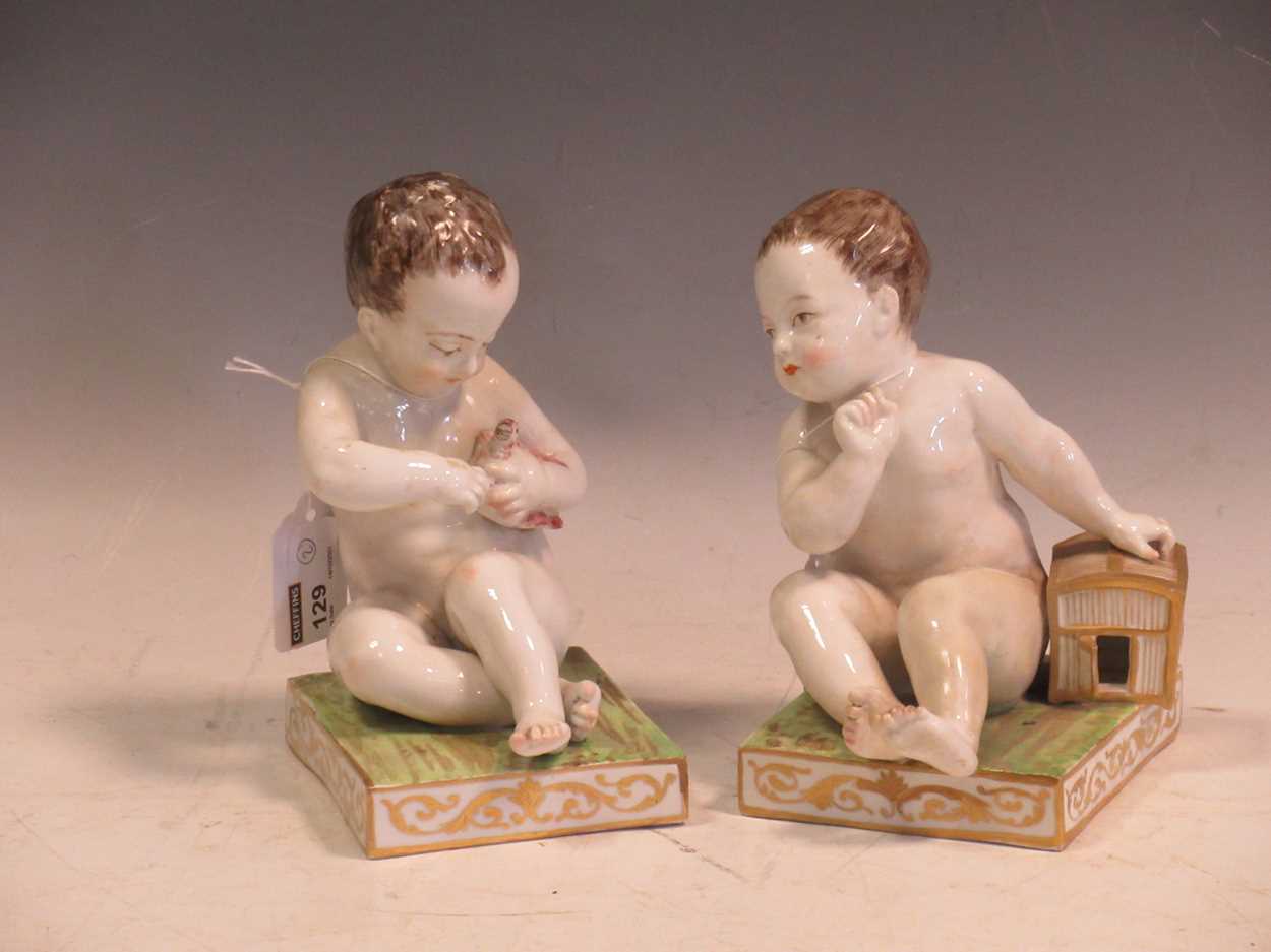 A pair of Meissen bookends, modelled as seated cherubs, the rectangular bases mounted with cages,