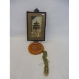 An Oriental glazed temple seal hanging from a framed print of a temple.