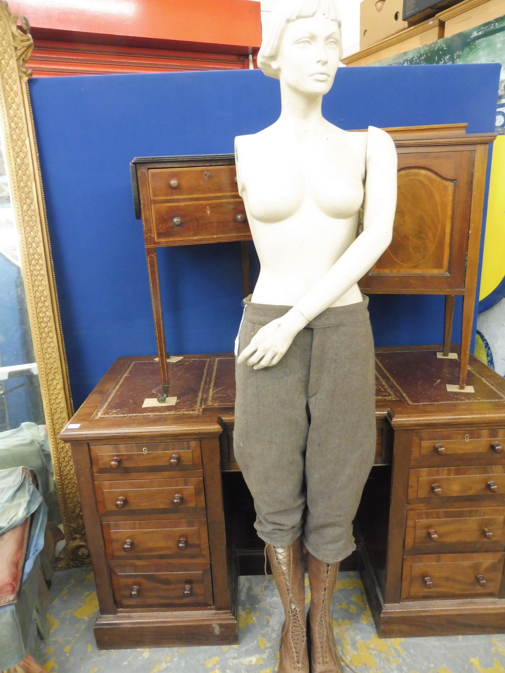 A one-armed female mannequin clothed from the waist down including tall brown leather lace up boots.