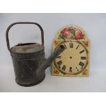 A wooden painted longcase clock face plus a watering can.