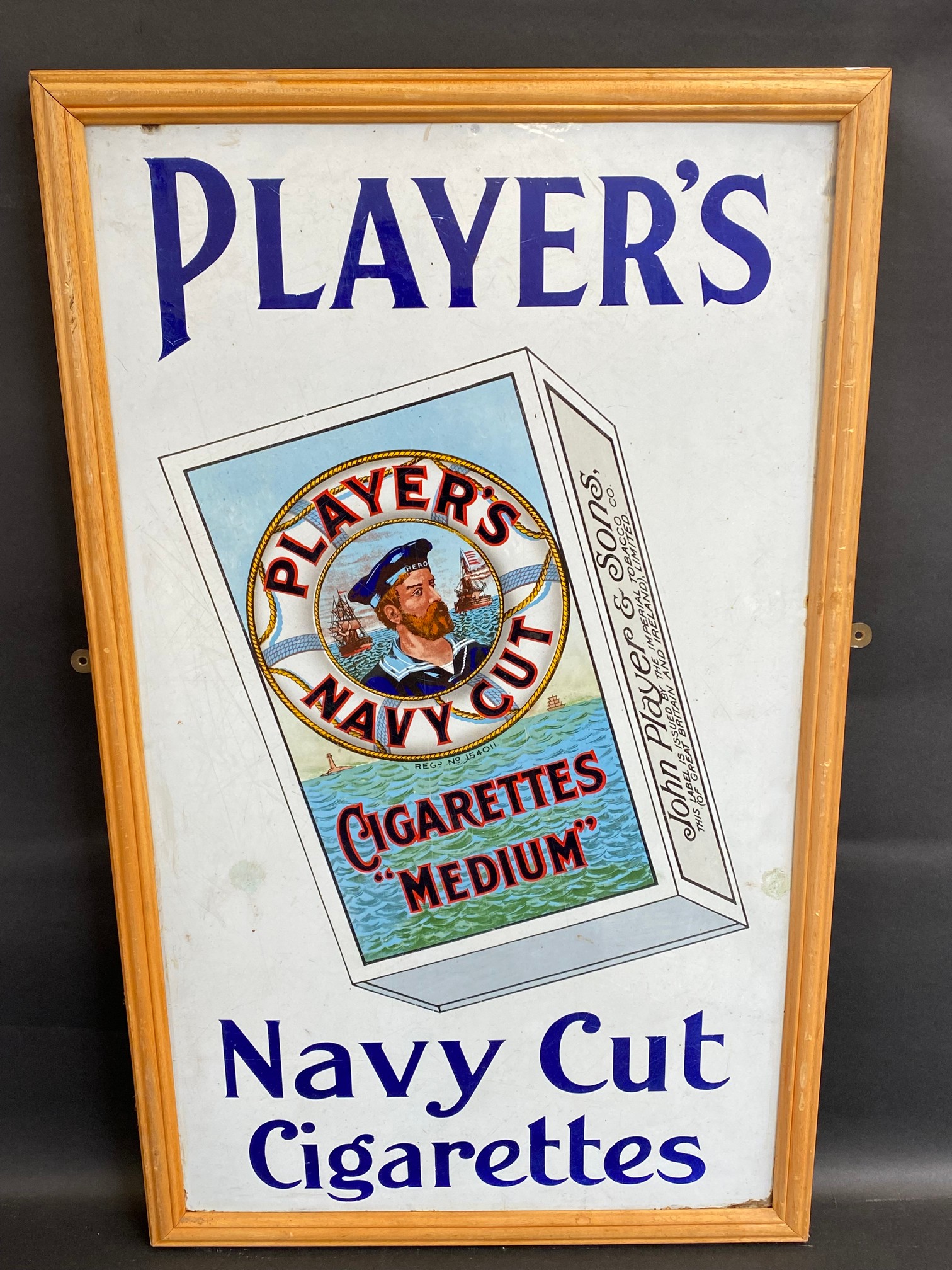 A Player's Navy Cut Cigarettes pictorial packet enamel sign in a frame, mounted on a board, two