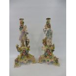 A pair of 19th Century Continental porcelain candlesticks, each stem with a standing figure, the