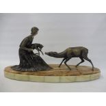 An Art Deco table top figure group of a lady holding a doe with a standing deer beside, sat on an