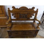 An early 20thC box seat Oak Settle, the two panel front with open scroll arms, foliate carved shaped