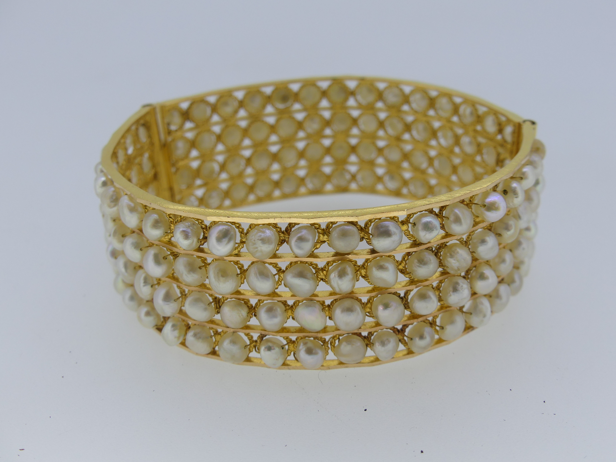 A hinged Bangle, formed of four rows of cultured pearls within a ropework frame, unmarked but tested