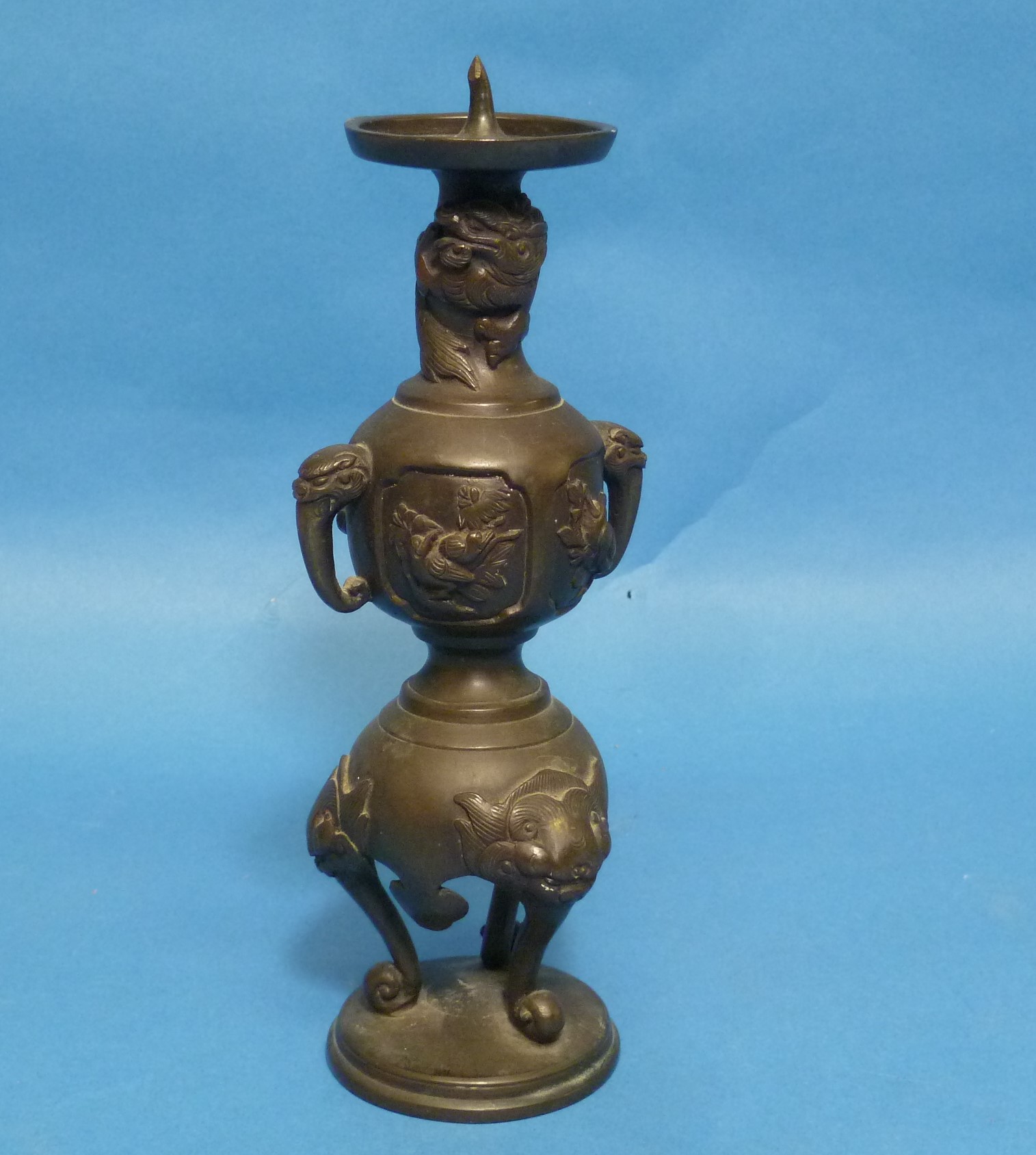 An antique Oriental bronze Candlestick, embossed in relief with three-toed dragons, dogs of Foo,