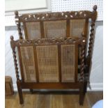 An early 20th century Carolean style carved oak single bed, with caned head board and foot board,