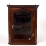 An early 19th Century oak corner cupboard enclosed by an arch top glazed door,