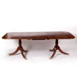 A mahogany two-pillar dining table with one extra leaf, on outswept reeded legs,