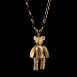 A novelty 9ct gold teddy bear pendant, with green set buttons to his front and jointed limbs,