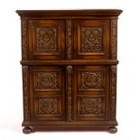 An oak cupboard enclosed by a pair of scroll carved panel doors above another pair of cupboard