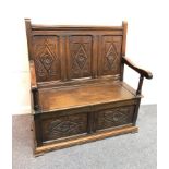 A 17th Century style oak settle with carved three-panel back, hinged seat on a carved box,