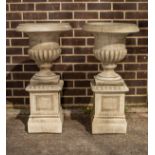 A pair of reconstituted stone garden vases on pedestal bases,