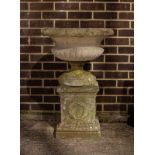A reconstituted stone garden vase with reeded base on a pedestal,