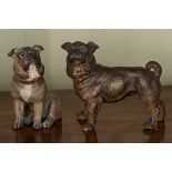 Two painted pottery figures of pugs, each with glass eyes, one standing, the other seated,